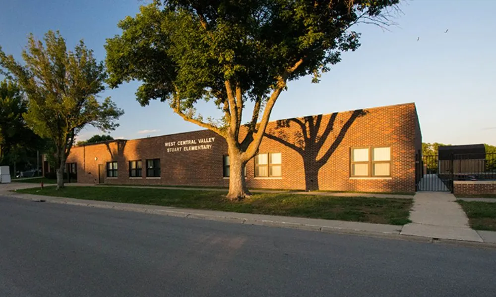 West Central Valley Stuart Elementary, a low brick school building with mature shade trees at golden hour.