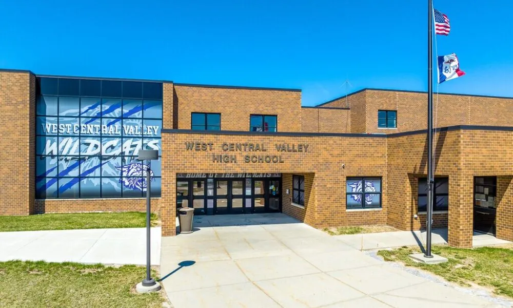 West Central Valley High School entrance under a blue sky, with the Wildcats mural and flags flying out front.