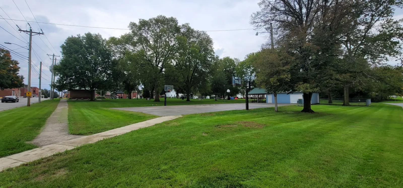 The playground at Redfield City Park with swings, slides, a climbing tunnel, and stepping stumps on a tree-shaded lawn