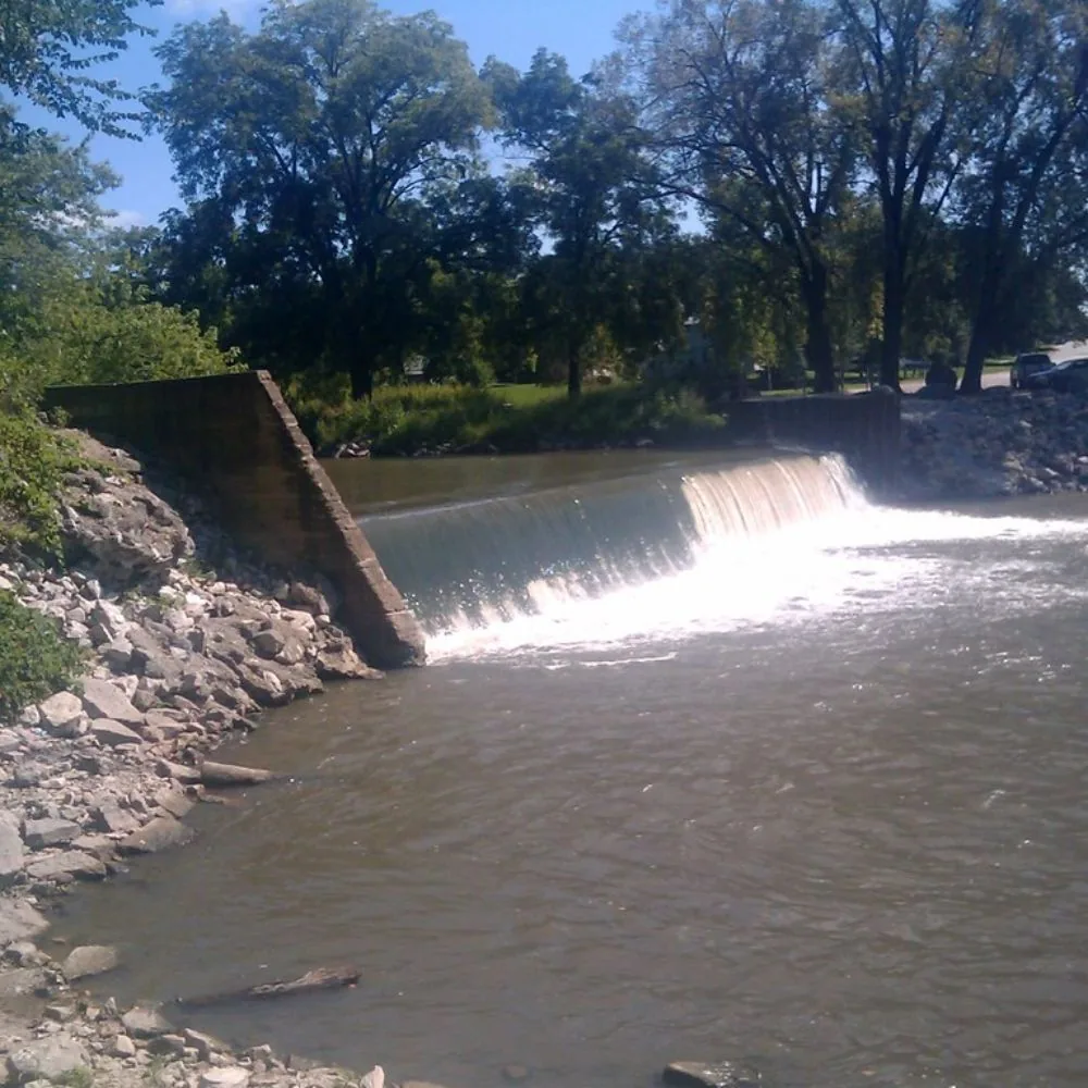 Water cascading over Redfield Dam beside the wooded banks of the Middle Raccoon River