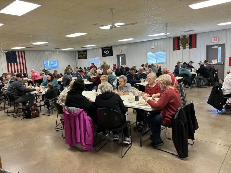 Neighbors filling tables in the Legion Hall dining room, decorated with an American flag and veterans banners, during the Saturday breakfast