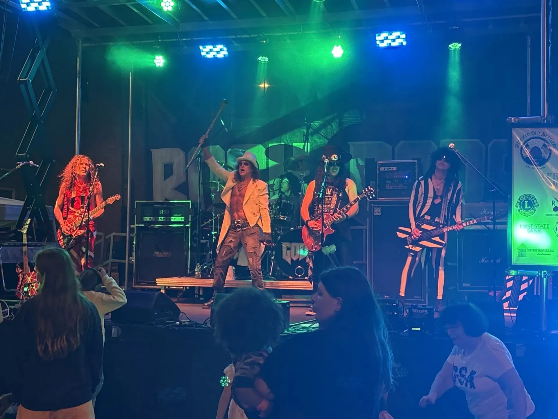 Costumed rock band performing under green and blue stage lights for the crowd at an Old Settlers Days evening concert in Redfield