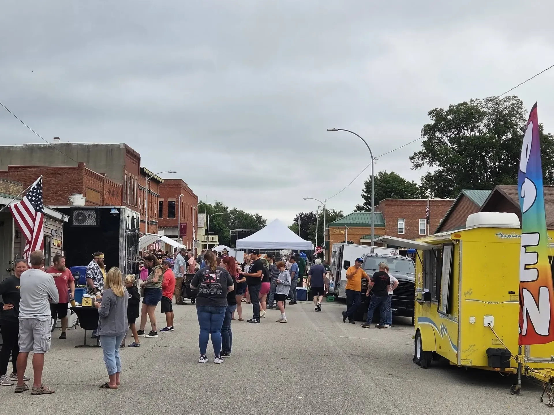 Crowds gathering among food trucks, vendor tents, and brick storefronts on downtown Redfield's main street during Old Settlers Days